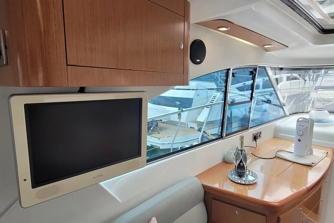 Contemporary yacht interior featuring a mounted TV, champagne bottle, and scenic views of boats through large windows.